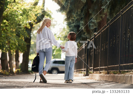 Rear view, walking. Schoolgirl with her mother are outdoors together 133263133