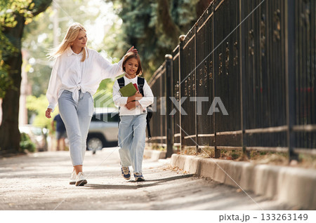 With books, front view. Schoolgirl with her mother are outdoors together With books, front view. Schoolgirl with her mother are outdoors together 133263149