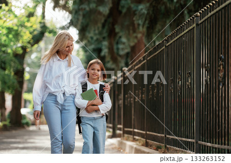 With books, front view. Schoolgirl with her mother are outdoors together With books, front view. Schoolgirl with her mother are outdoors together 133263152