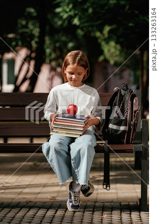 An apple on the books. Schoolgirl is sitting on the bench outdoors 133263164