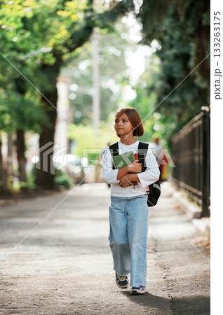Holding notepad. Schoolgirl with backpack is outdoors 133263175