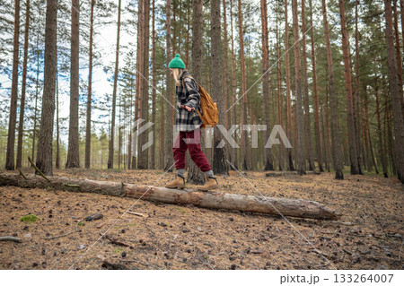 Smiling woman on fallen tree trunk in woods. Playful hiker balancing in quiet forest alone 133264007