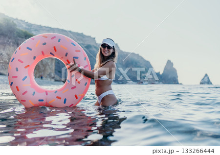 Woman donut beach. Happy woman smiles holding donut inflatable in ocean water during summer vacation. 133266444