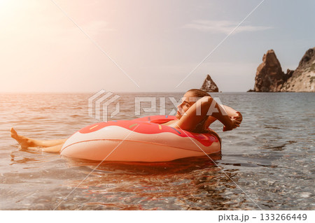 Woman Inflatable Float - Relaxing in ocean on a pink donut float during summer vacation. Woman Inflatable Float - Relaxing in ocean on a pink donut float during summer vacation. 133266449