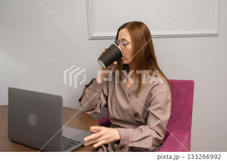 Businesswoman remote work coffee break. Professional drinking from cup while typing on laptop. 133266992