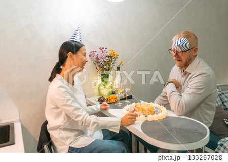 Birthday Surprise Party Indoor Elderly Man Woman: Happy woman surprises a blindfolded elderly man with a birthday cake indoors; celebrating a birthday. Birthday Surprise Party Indoor Elderly Man Woman: Happy woman surprises a blindfolded elderly man with a birthday cake indoors; celebrating a birthday. 133267028