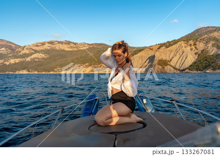 Woman, boat, vacation. Young woman kneeling on a boat enjoying the sea view and mountains during a golden hour cruise. Woman, boat, vacation. Young woman kneeling on a boat enjoying the sea view and mountains during a golden hour cruise. 133267081