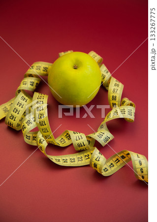 Fresh green apple on a red backdrop, encircled by a measuring tape, representing health and nutrition, highlighting the significance of mindful eating and healthy living Fresh green apple on a red backdrop, encircled by a measuring tape, representing health and nutrition, highlighting the significance of mindful eating and healthy living 133267775