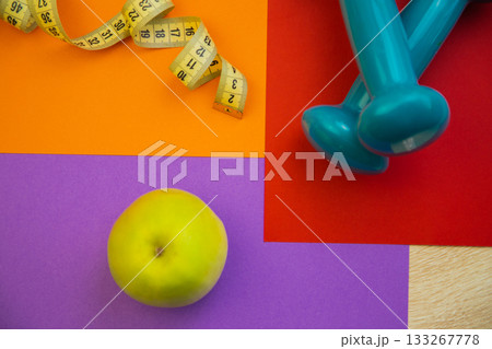 Fresh green apple on colorful surface with measuring tape and dumbbells, representing healthy living, fitness goals, and wellness choices in a vibrant setting Fresh green apple on colorful surface with measuring tape and dumbbells, representing healthy living, fitness goals, and wellness choices in a vibrant setting 133267778