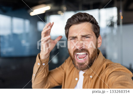 Furious businessman shouting in an office, overwhelmed by stress and frustration, mouth wide open as he vents anger and exhaustion from work pressure and burnout 133268354