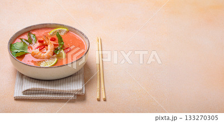 Traditional Thai soup tom yum soup with shrimp, lime, and herbs in bowl with chopsticks on light beige background, space for text Traditional Thai soup tom yum soup with shrimp, lime, and herbs in bowl with chopsticks on light beige background, space for text 133270305