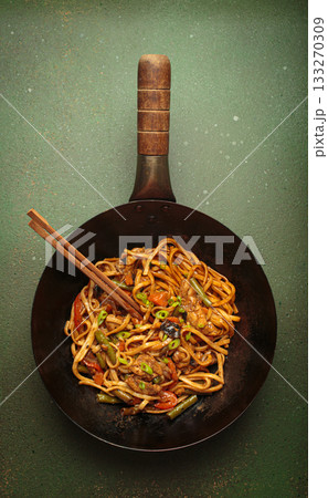 Asian style stir fry noodles with chicken and vegetables in a black wok pan with chopsticks Asian style stir fry noodles with chicken and vegetables in a black wok pan with chopsticks 133270309