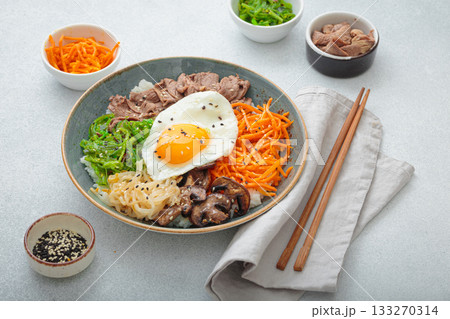 Traditional korean bibimbap with fried egg, beef and vegetables and other toppings on light background with chopsticks 133270314
