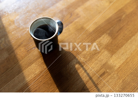 伸びるコーヒーカップの影と机 133270655