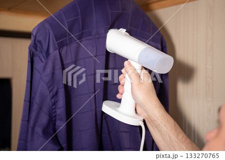 Steamer Smoothing Purple Shirt on Hanger in Room Setting Steamer Smoothing Purple Shirt on Hanger in Room Setting 133270765