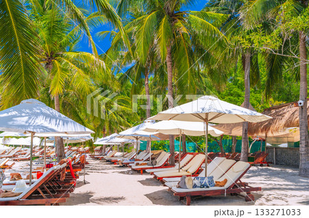 sun umbrellas and beds on sandy beach under palm trees at a luxury seaside resort in summer. Beach by sea on tropical exotic island in Asia. Tourist holidays and travel 133271033