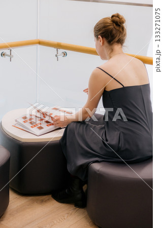 woman in library is reading book sitting on wide chair. lady in black dress flips through pages. woman in library is reading book sitting on wide chair. lady in black dress flips through pages. 133271075