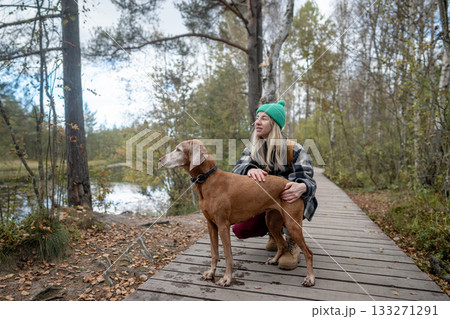 Pleased woman petting and holding hunting dog spot something near lake on eco trail in park 133271291