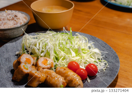 豚肉の野菜巻きと千切りキャベツ、雑穀ごはんと味噌汁の家庭的な夕食 133271404