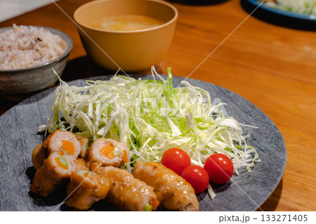 豚肉の野菜巻きと千切りキャベツ、雑穀ごはんと味噌汁の家庭的な夕食 133271405