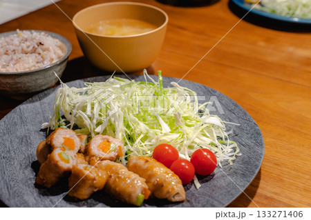 豚肉の野菜巻きと千切りキャベツ、雑穀ごはんと味噌汁の家庭的な夕食 133271406
