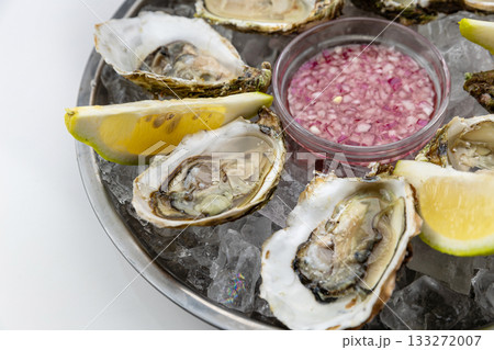 Closeup of fresh oysters on ice with lemon wedges and mignonette, seafood detail 133272007