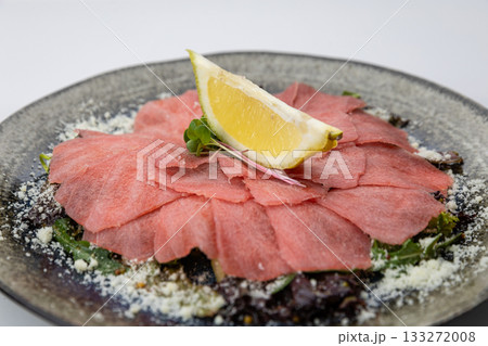 Tuna carpaccio with lemon and parmesan on greens, black plate, studio top view Tuna carpaccio with lemon and parmesan on greens, black plate, studio top view 133272008