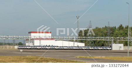A vast outdoor storage lot at an automotive factory is filled with rows of brand-new, white cars A vast outdoor storage lot at an automotive factory is filled with rows of brand-new, white cars 133272044