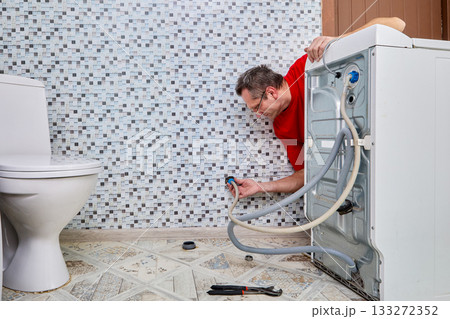 Worker secures inlet hose by hand onto water pipe connection protruding from wall, ensuring firm attachment to water source for washing machine. Worker secures inlet hose by hand onto water pipe connection protruding from wall, ensuring firm attachment to water source for washing machine. 133272352