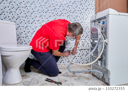 Specialist hand connects water supply hose to wall pipe fitting supplying water for washing machine operation. Specialist hand connects water supply hose to wall pipe fitting supplying water for washing machine operation. 133272355