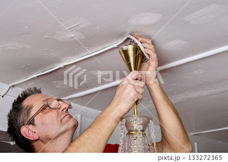 Technician disconnects old crystal chandelier, loosening ceiling mount in rural home, handling fixture carefully. 133272365