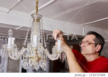 Removal process demonstrates technician taking out bulbs from crystal chandelier before lifting entire piece off ceiling in country home. 133272366