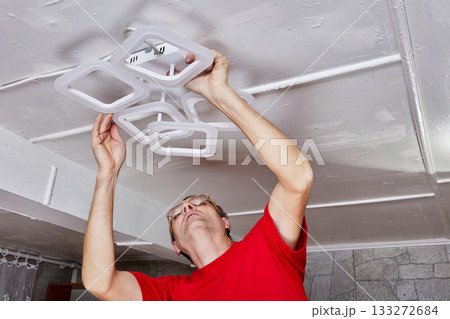 Mounting process involves technician fixing LED chandelier to ceiling during installation task in country home ensuring electrical connection. 133272684