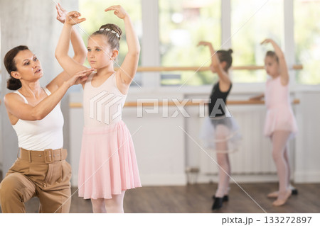 Woman teacher choreographer patiently teaches little girls the basics of ballet Woman teacher choreographer patiently teaches little girls the basics of ballet 133272897