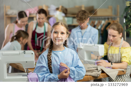 Teenage girl happily shows off a t-shirt he sewed with his own hands on sewing machine Teenage girl happily shows off a t-shirt he sewed with his own hands on sewing machine 133272969