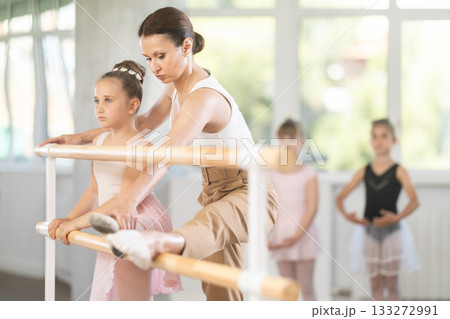Woman teacher helps girl stretch at barre 133272991