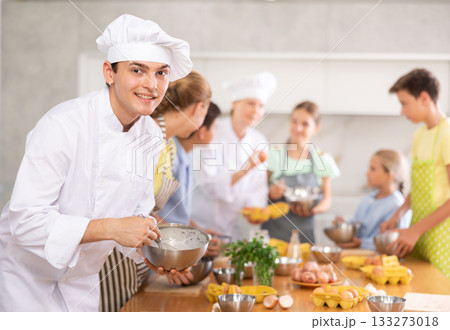 Portrait of positive chef teaching how to beat eggs and prepare dough in cooking class for teenage kids Portrait of positive chef teaching how to beat eggs and prepare dough in cooking class for teenage kids 133273018
