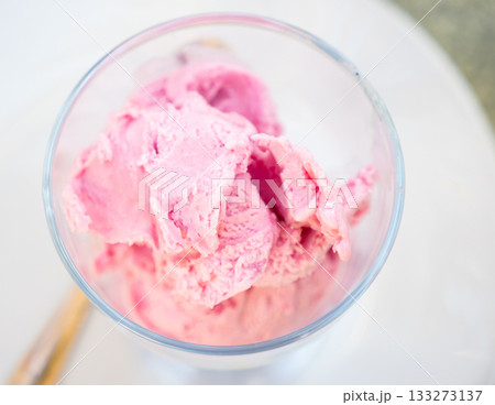 Serving of strawberry ice cream is perform in clear glass cup 133273137