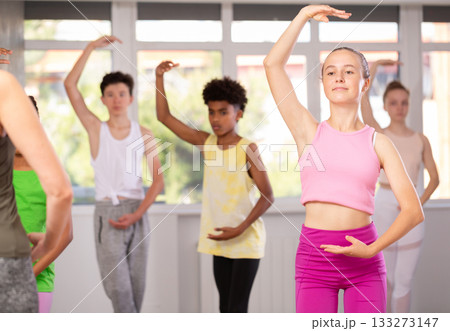 Positive teenage girl practicing ballet positions standing in row with others Positive teenage girl practicing ballet positions standing in row with others 133273147