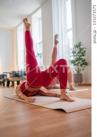 Pilates women performing inverted leg raises, pair of women practicing inverted leg raises with focus on the buttocks 133273575