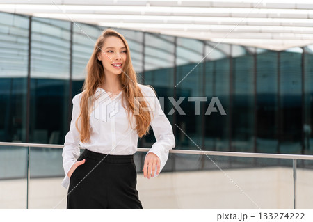 Smiling businesswoman in white shirt standing by 133274222