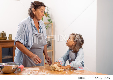 Girl baking with grandmother kneading dough on 133274225