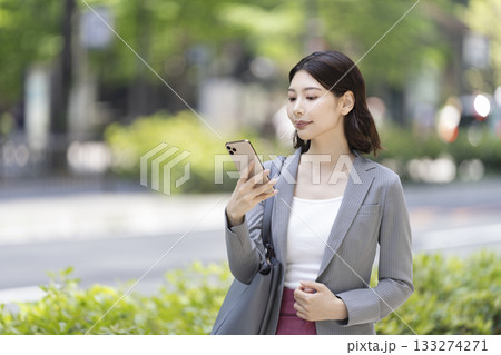 外出先でスマートフォンの画面を見るビジネスウーマン 外出先でスマートフォンの画面を見るビジネスウーマン 133274271