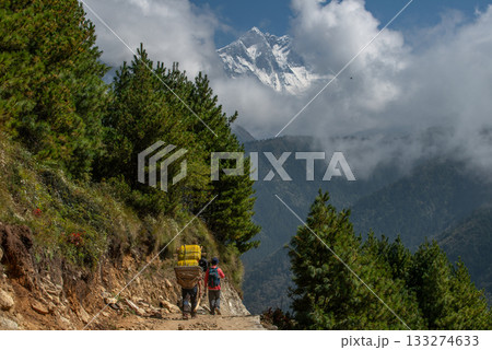 Rear view of tourist and porter trekking in Sagarmatha national park, Nepal with beautiful view of Mt.Lhotse (8,516 m) rising behind the clouds. 133274633
