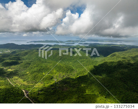Lush green mountain range covered with forest under cloudy sky and sunlight patches. Siargao, Philippines. 133275034