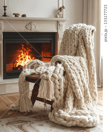 暖炉のそばの椅子に掛けられた、温かそうなニットのブランケット 133277725