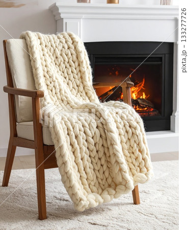 暖炉のそばの椅子に掛けられた、温かそうなニットのブランケット 133277726