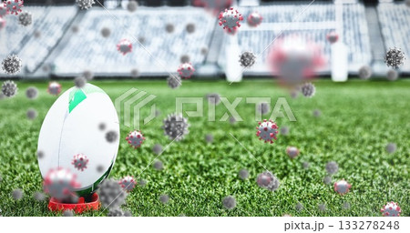 Resting rugby ball on red kicking tee at stadium pitch with floating coronavirus models, copy space 133278248