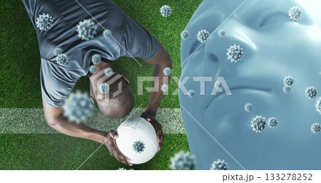 Gripping rugby ball athlete in sportswear crouching on field, with virus, head overlay, copy space 133278252