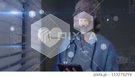 Holding tablet, scrub nurse analyzing beside blinds in corridor, with stethoscope and health icons Holding tablet, scrub nurse analyzing beside blinds in corridor, with stethoscope and health icons 133278259